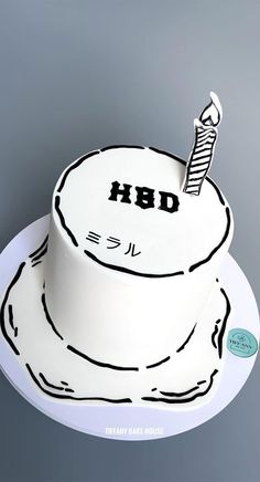 a white cake with black writing on it and a candle sticking out of the top