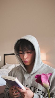 a young man sitting on a bed reading a book with a flower in front of him