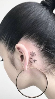 a woman's ear has a small rose tattoo on her left behind the ear