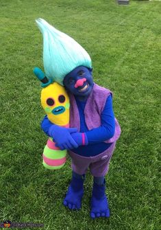 a person in blue and purple holding a stuffed animal on green grass with other items