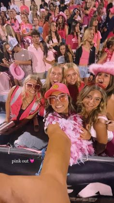 a group of women in pink hats and sunglasses taking a selfie at a sporting event