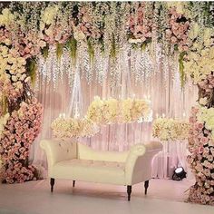 a white couch sitting in front of a flower covered stage with chandeliers and flowers