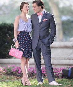 a man in a suit and tie standing next to a woman wearing a pink purse