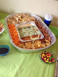 a party platter with chips, dip and veggies in it on a green table cloth