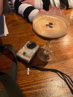 a camera sitting on top of a wooden table next to a glass filled with liquid