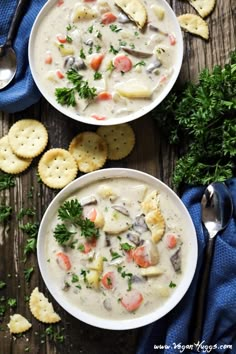 two bowls filled with soup next to crackers and parsley on a wooden table