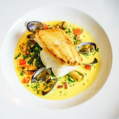 a white plate topped with fish and mussels on top of broth covered in sauce