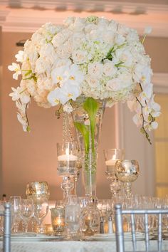 a vase filled with white flowers sitting on top of a table covered in glasses and candles