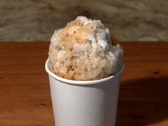 a small white cup filled with sugar on top of a wooden table next to a wall