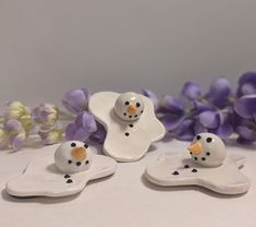 three ceramic snowmen sitting on top of each other in front of purple and white flowers