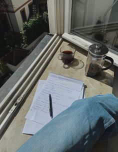 a person sitting at a window sill writing on a piece of paper