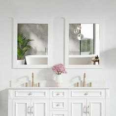 a white bathroom with two mirrors above the sinks and flowers in vase on the counter