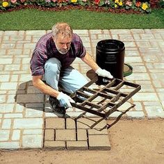 a man kneeling down next to a black trash can on top of a brick walkway