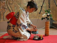 a woman is sitting on the floor and pouring tea from a pot into a cup