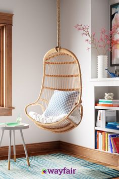 a hanging chair in the corner of a room next to a table and bookshelf