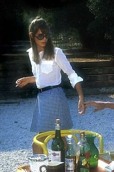 a woman standing in front of a picnic table filled with bottles and glasses on it