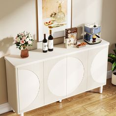 a white sideboard with two wine bottles and flowers on it in front of a painting