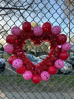 a heart shaped wreath hanging on a fence with pink and red balls in the shape of a heart