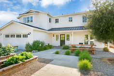 a white house with lots of plants in the front yard and an outdoor picnic table