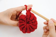 two hands holding knitting needles and crochet red flower ornament on white background