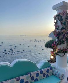 an outdoor seating area overlooking the ocean with boats in the water and flowers growing on it