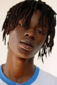 a close up of a person with dreadlocks on their head and wearing a blue shirt