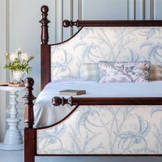 a bed with blue and white wallpaper next to a table with flowers on it