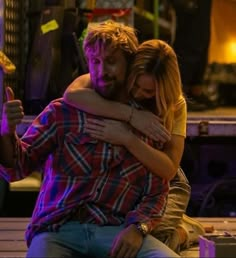 a man and woman hugging each other on a bench in front of a purple light