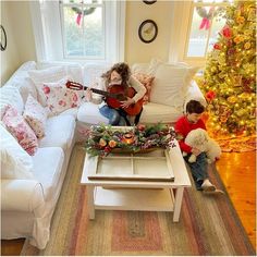 a woman playing the guitar while sitting on a couch next to a child with a teddy bear