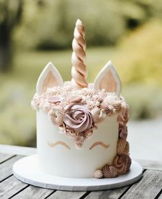 a white cake with pink frosting and a unicorn's horn on top is sitting on a wooden table