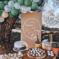 a table topped with cake and cupcakes next to a tree filled with balloons