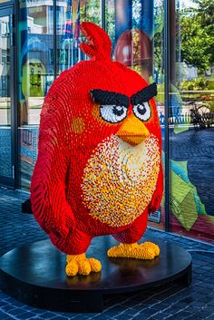 a red lego angry bird on display in front of a building with glass doors and windows