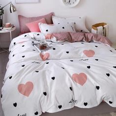 a bed with pink and black hearts on the comforter in a white room next to a clock