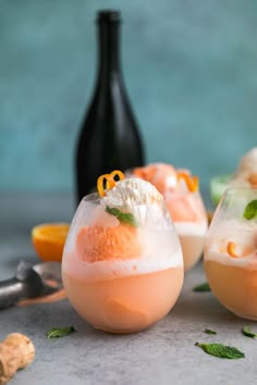 two glasses filled with ice cream and orange garnish next to a bottle of wine