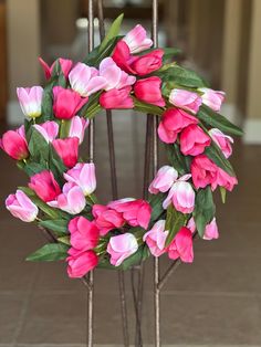 a wreath with pink and white tulips hanging on a metal stand in front of a door