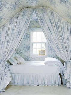 a white bed sitting next to a window in a room with curtains on the windowsill