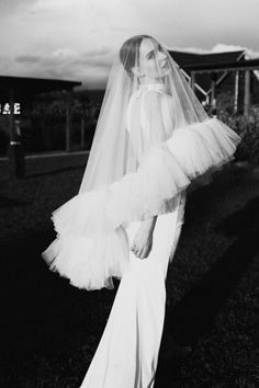 black and white photo of woman in wedding dress with veil over her head standing on grass