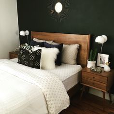 a bedroom with green walls and white bedding, black accent pillows and wooden headboard