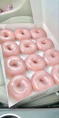 a box filled with pink frosted donuts on top of a car seat