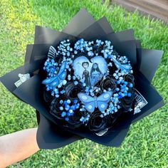 a bouquet made out of black paper with blue flowers and pictures on the top, in someone's hand