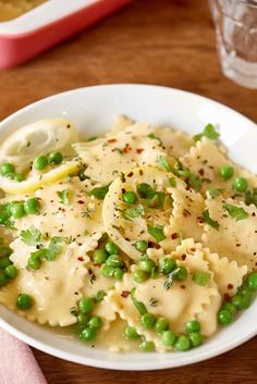 a white bowl filled with pasta and peas on top of a wooden table next to a fork