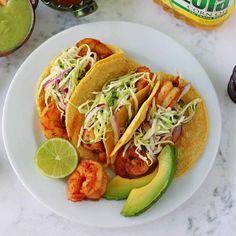 two tacos with shrimp, avocado and cilantro on a white plate