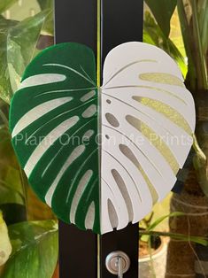 a green and white leaf is hanging on a black pole in front of some potted plants