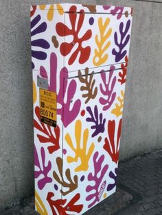 a painted box sitting on the sidewalk next to a wall with a tag in it