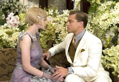 a man in a white suit sitting next to a woman on a couch with flowers