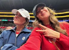 two women are sitting in the stands at a baseball game and one is pointing her finger