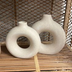 two white vases sitting next to each other on a bamboo mat in front of a basket