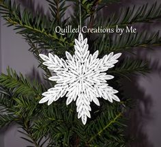 a white snowflake ornament hanging from a pine tree with the words quilted creations by me