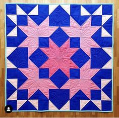 a blue and pink quilt with white stars on the center, in front of a wooden floor