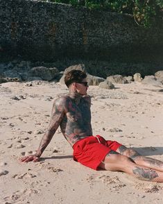 a man with tattoos laying on the beach